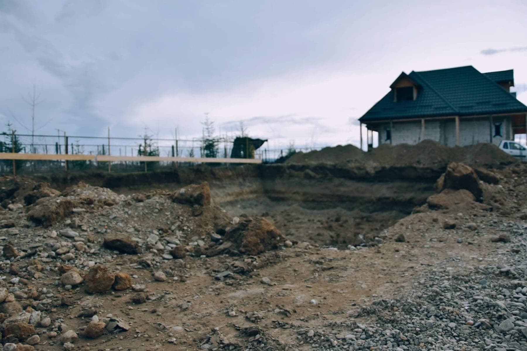 Săpături pentru fundație, la începutul construcției, cu o clădire ridicată în fundal